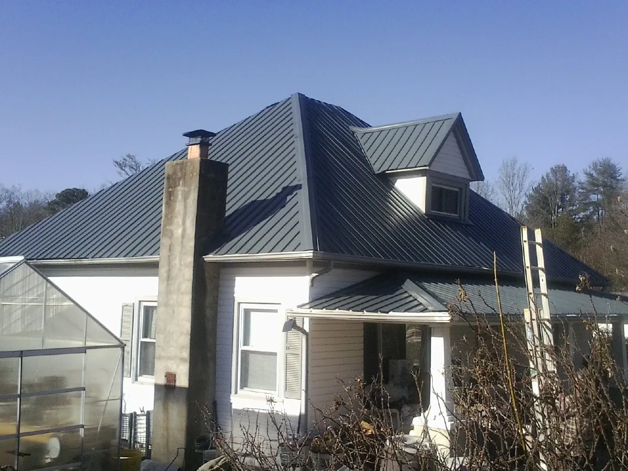 Dark blue standing seam metal roof on a white farmhouse with dormer — Slate & Tile Roof Repair by Roofing Brothers in Cummington