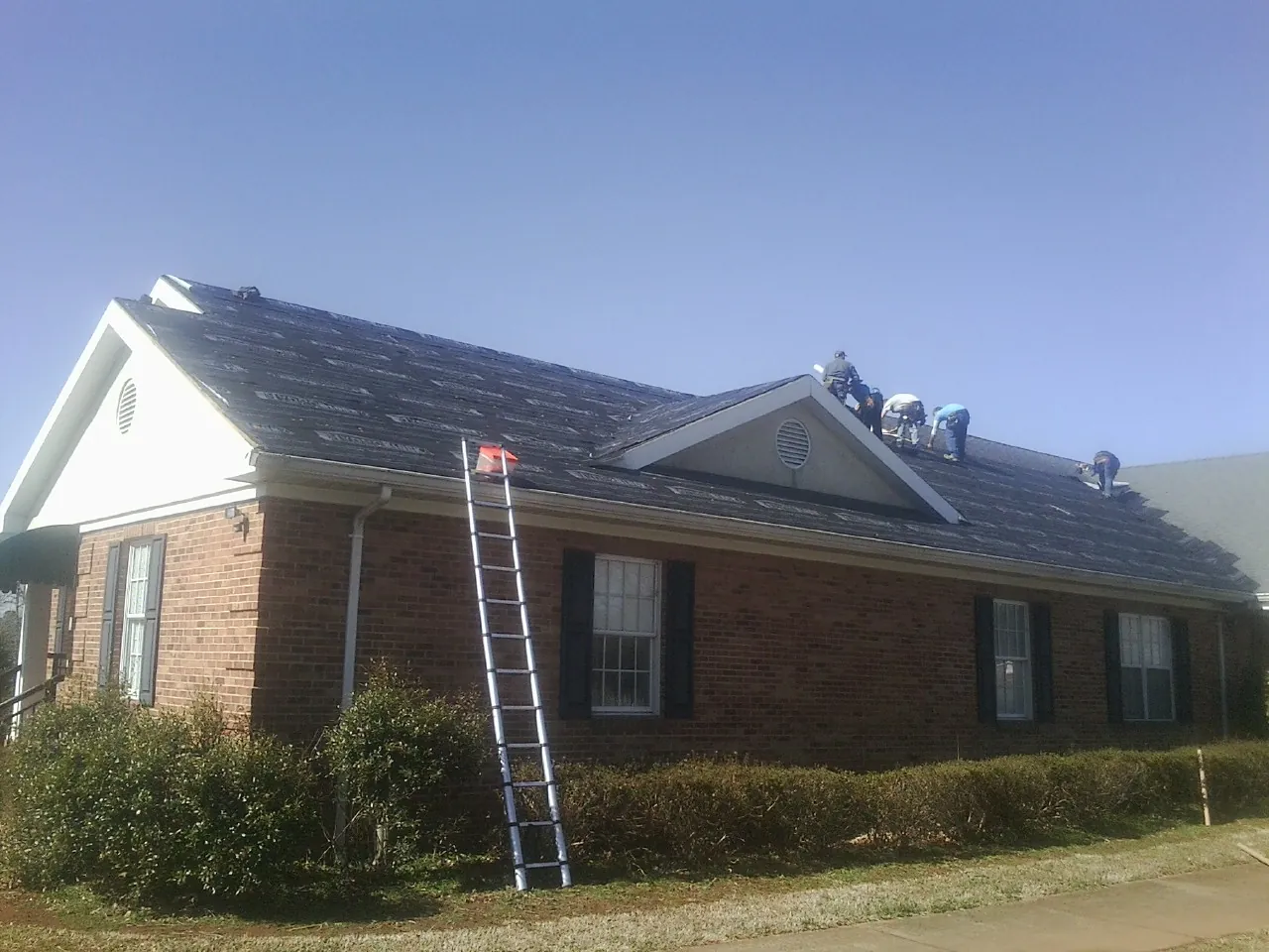 Crew tearing shingles off a brick ranch roof with a ladder set — Metal Roof Repair work by our crew in Cummington