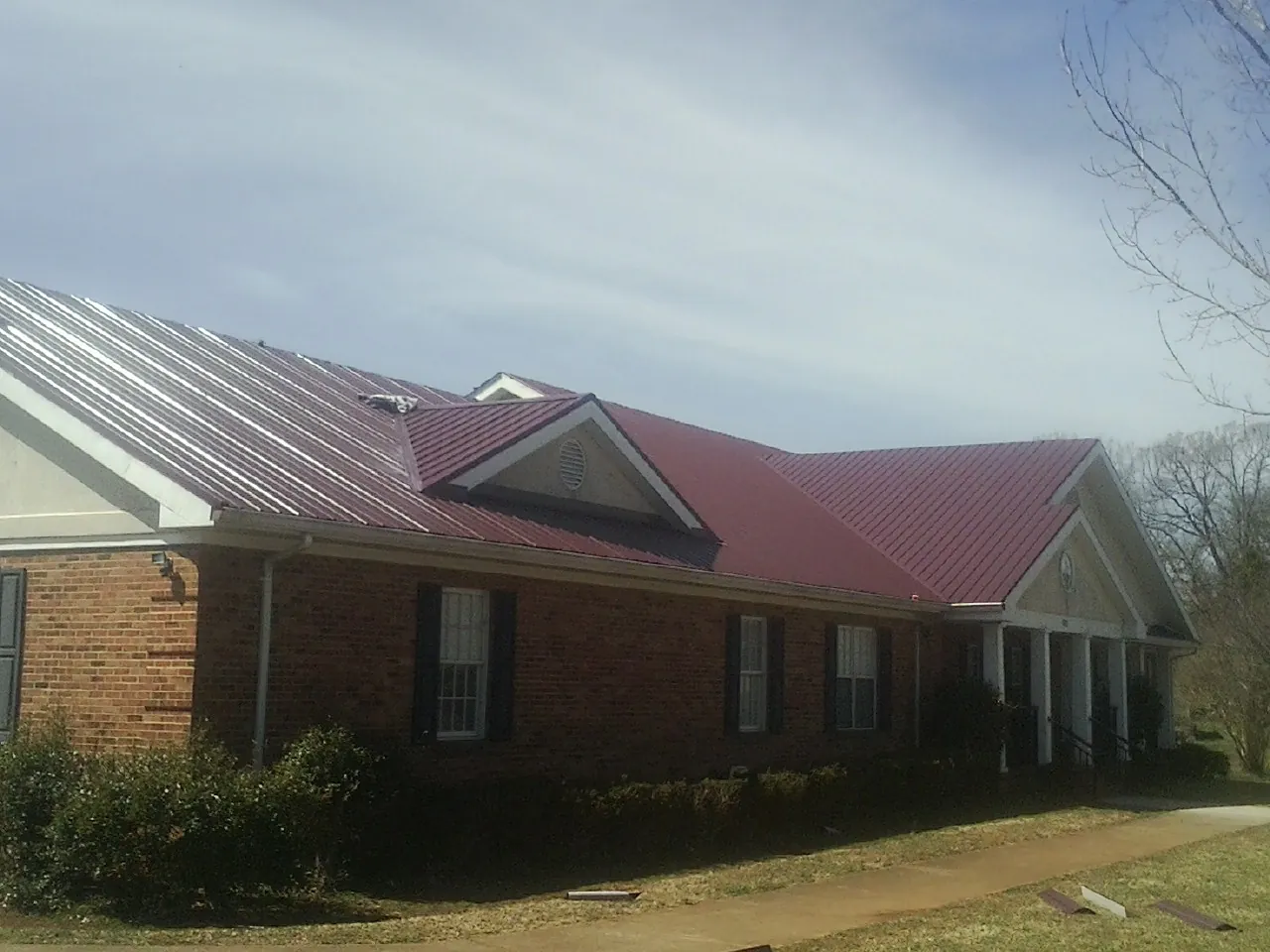 Red metal roof with gabled entries on a long brick building, from a Hail Damage Roof Repair job in Cummington