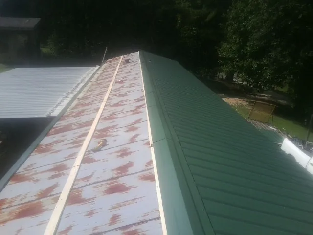Old rusted panels beside newly installed green metal roofing — Wind Damage Roof Repair by Roofing Brothers in Cummington