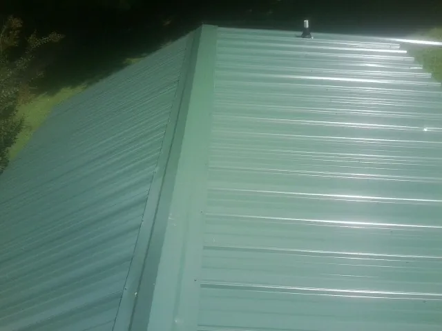 New green metal panels meeting at the ridge of a roof — Flat Roof Repair work by our crew in Cummington