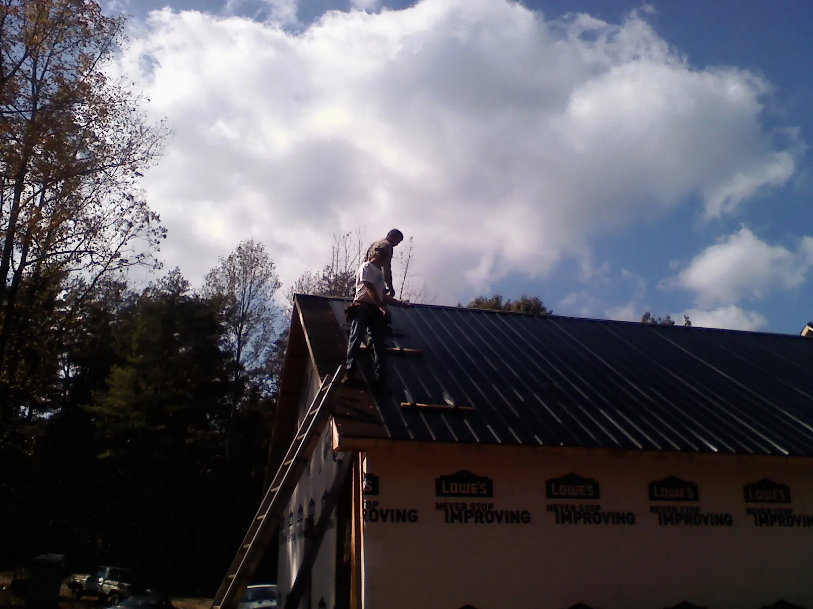 Roofer fastening dark metal panels high against a cloudy sky, from a Roof Inspection job in Cummington
