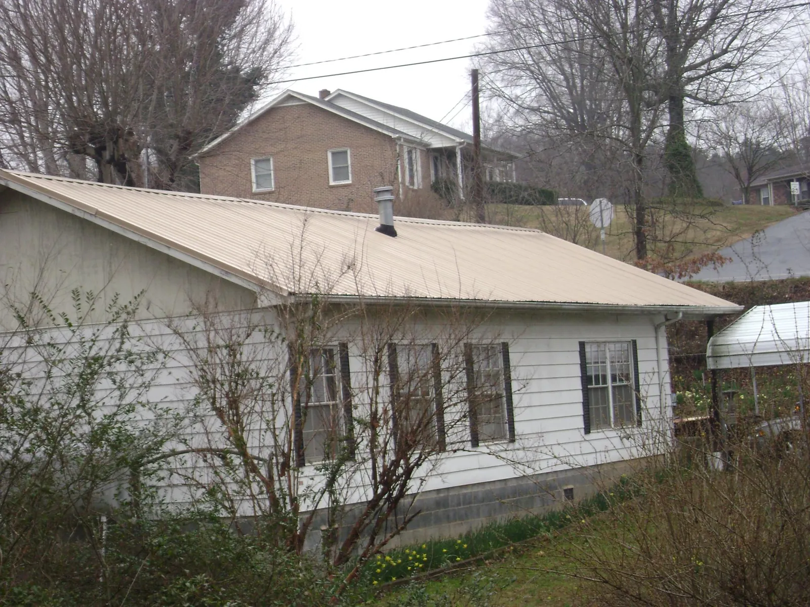 Tan metal roof on a white sided house set into a hillside — Commercial Roofing by Roofing Brothers in Cummington