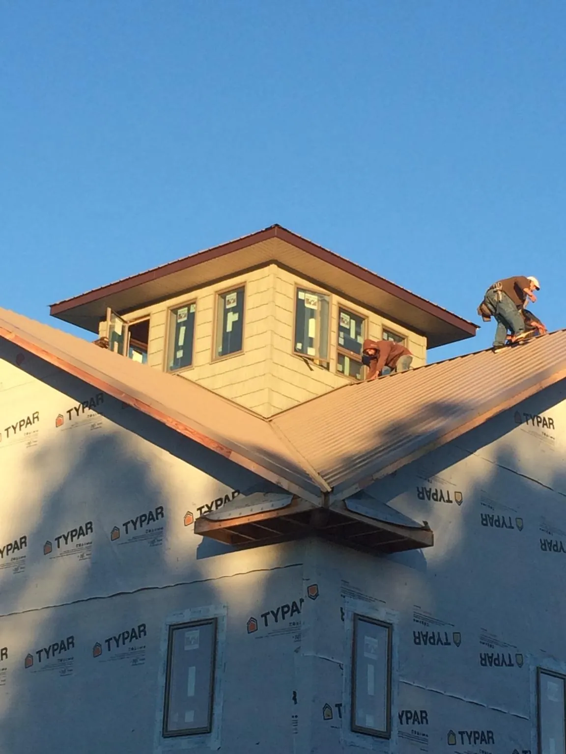 Roofers working around a rooftop cupola on a new metal roof at sunset — Roof Waterproofing in Cummington by Roofing Brothers